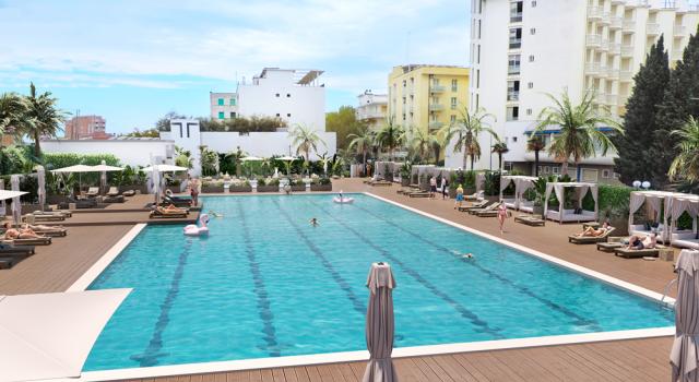 Piscina all'aperto con lettini e palme, circondata da edifici.